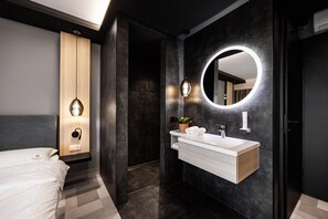 A modern bathroom with a vanity, mirror, and a bed in the adjacent room.
