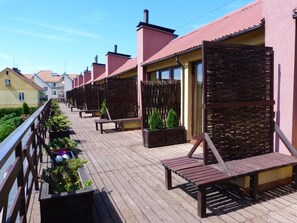 A wooden deck with outdoor seating and planters, surrounded by buildings with red roofs.