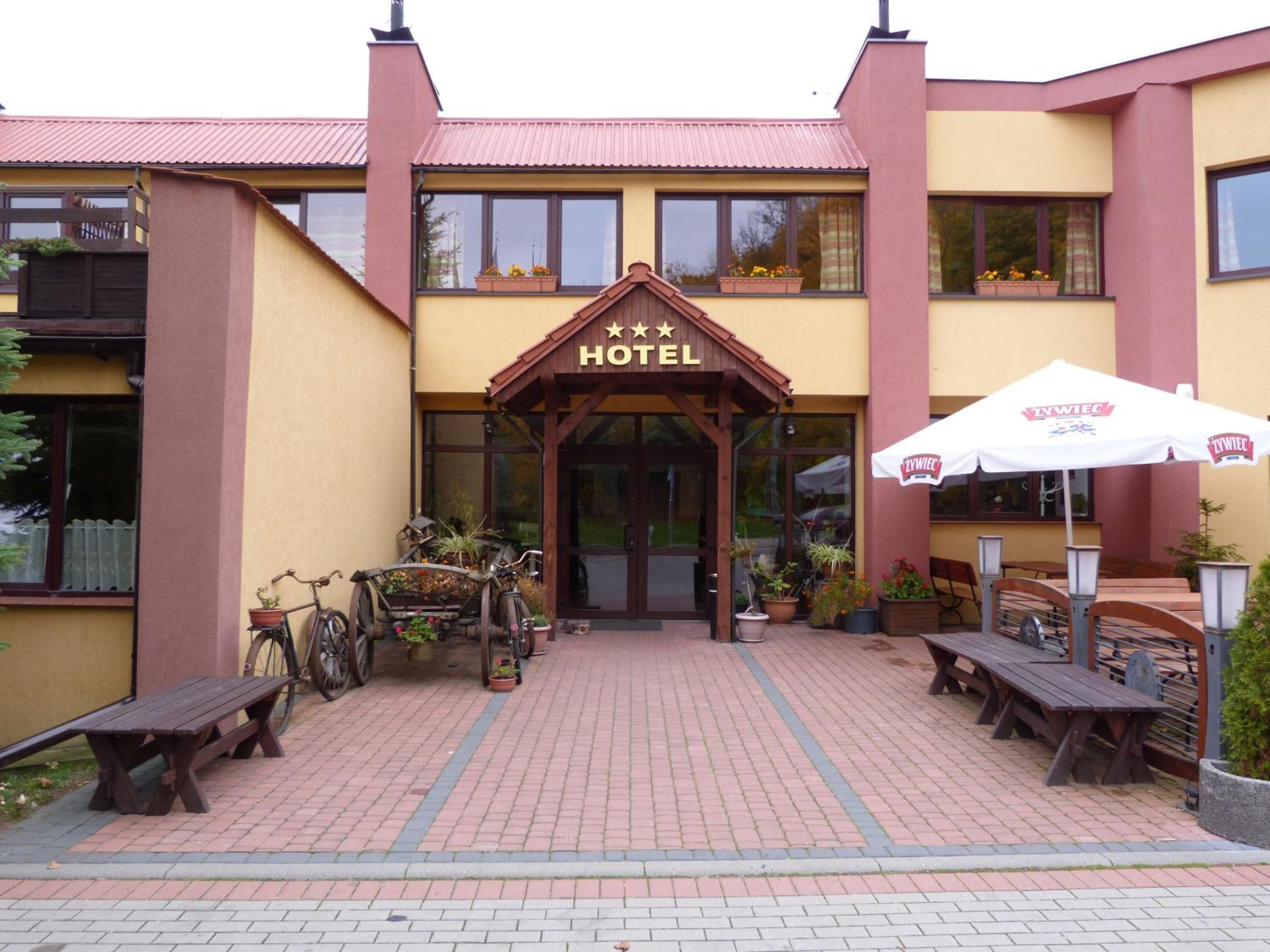 A hotel entrance with a sign, outdoor seating, and potted plants.