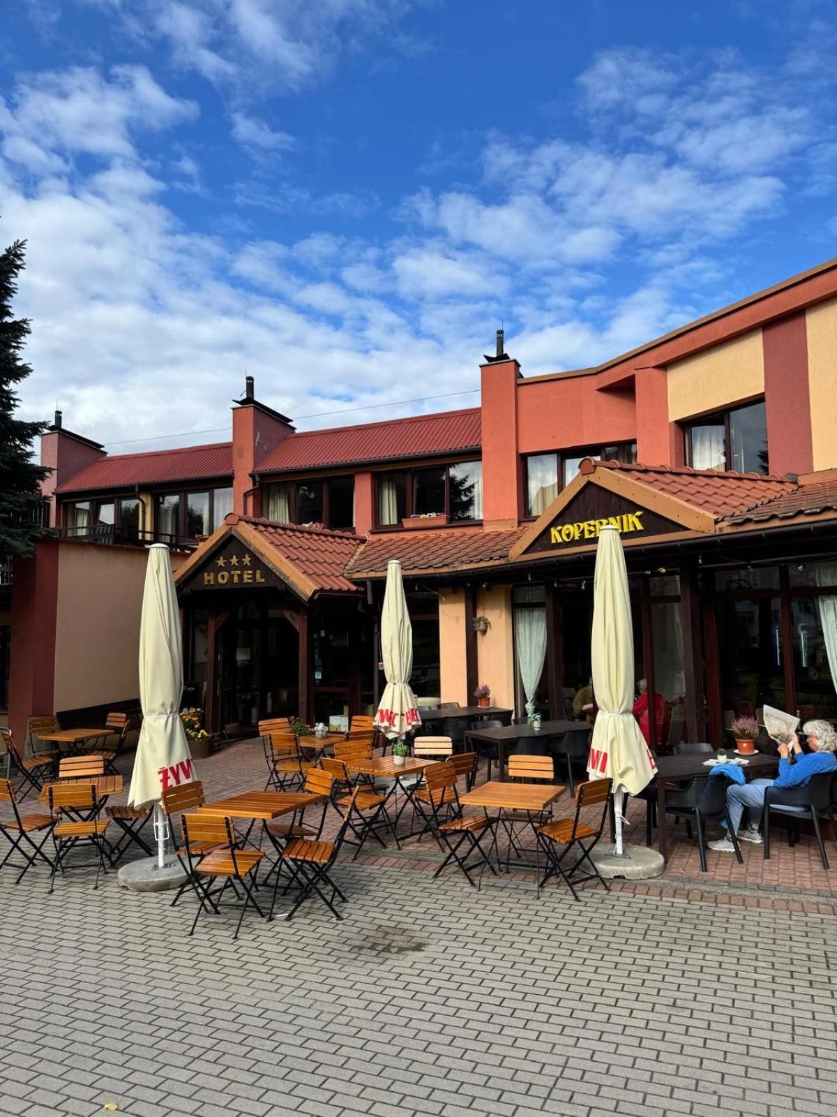 An outdoor seating area with tables and chairs, a hotel sign, and a building with a red facade.