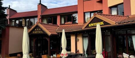 An outdoor seating area with tables and chairs, a hotel sign, and a building with a red facade.