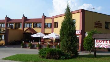A hotel with a yellow facade, a signboard, outdoor umbrellas, and a well-maintained garden.