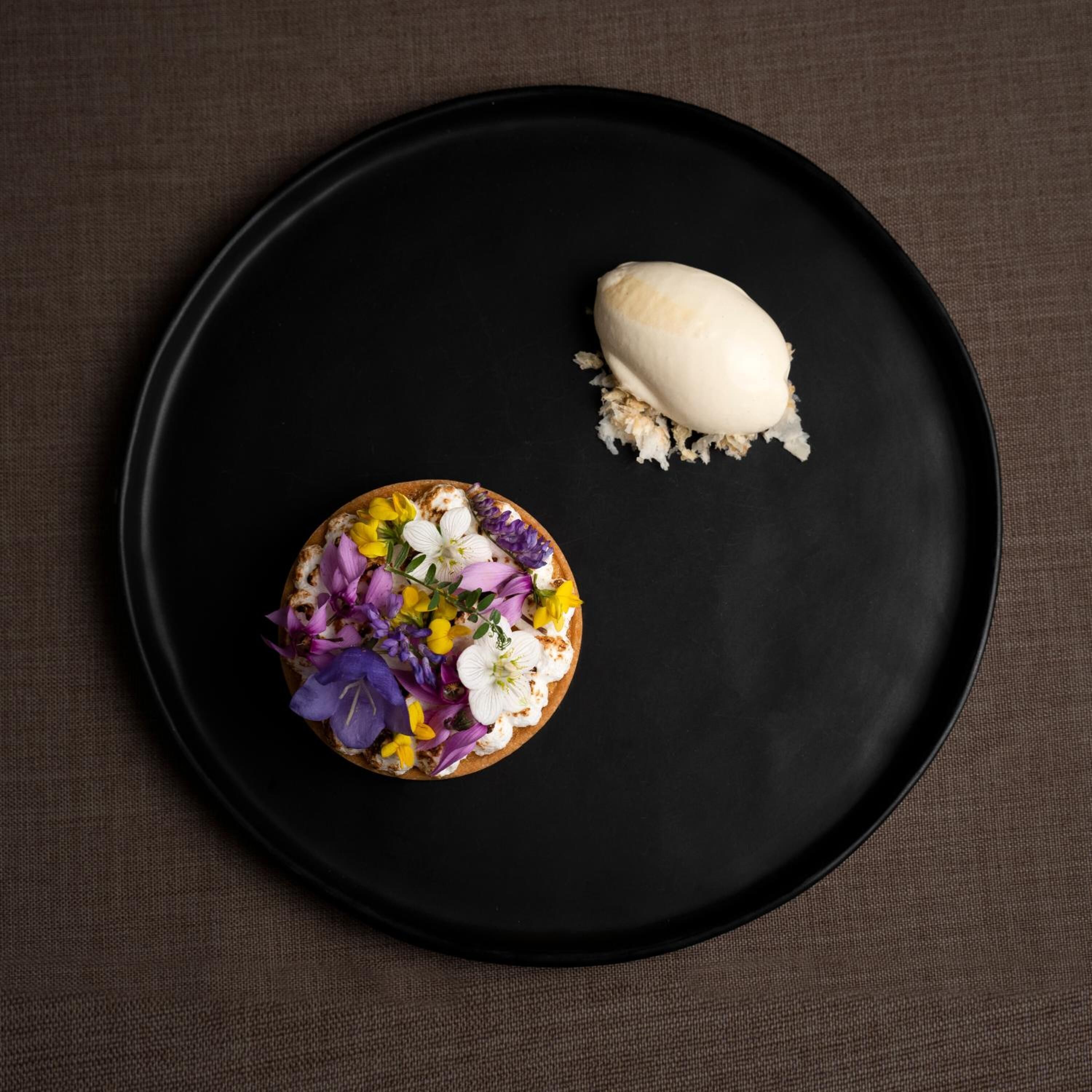 Een dessert op een zwart bord met bloemdecoratie en een bol ijs.