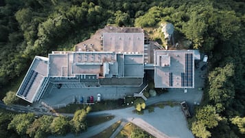 Vista aérea de un edificio con varias secciones, que incluye un área de estacionamiento con varios autos, paneles solares en los techos y un tanque de agua grande.
