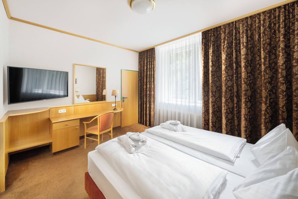 A hotel room with a bed, a desk, a chair, a television, and a window with curtains.