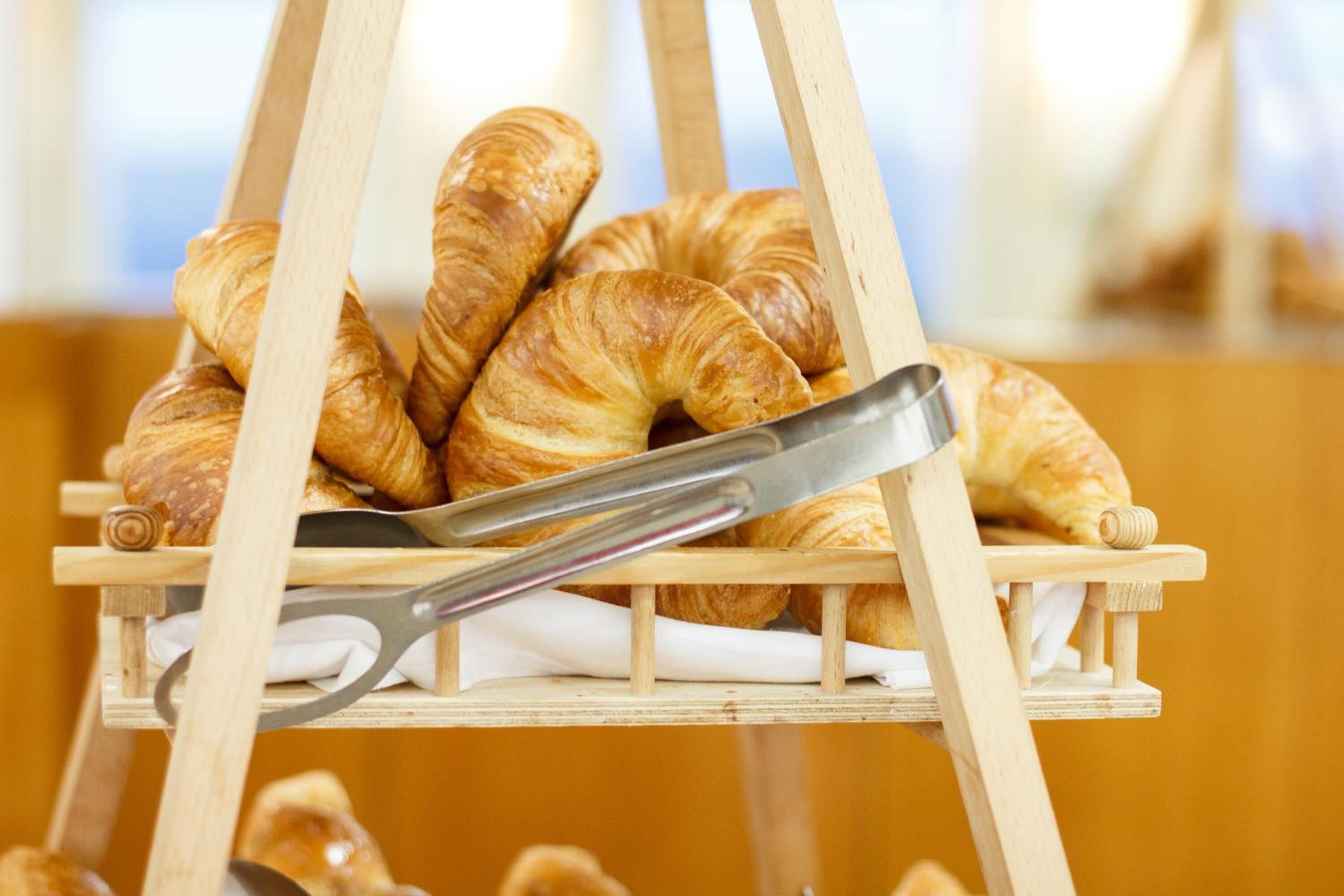 Een houten plank met meerdere croissants, met een paar tangen er bovenop.