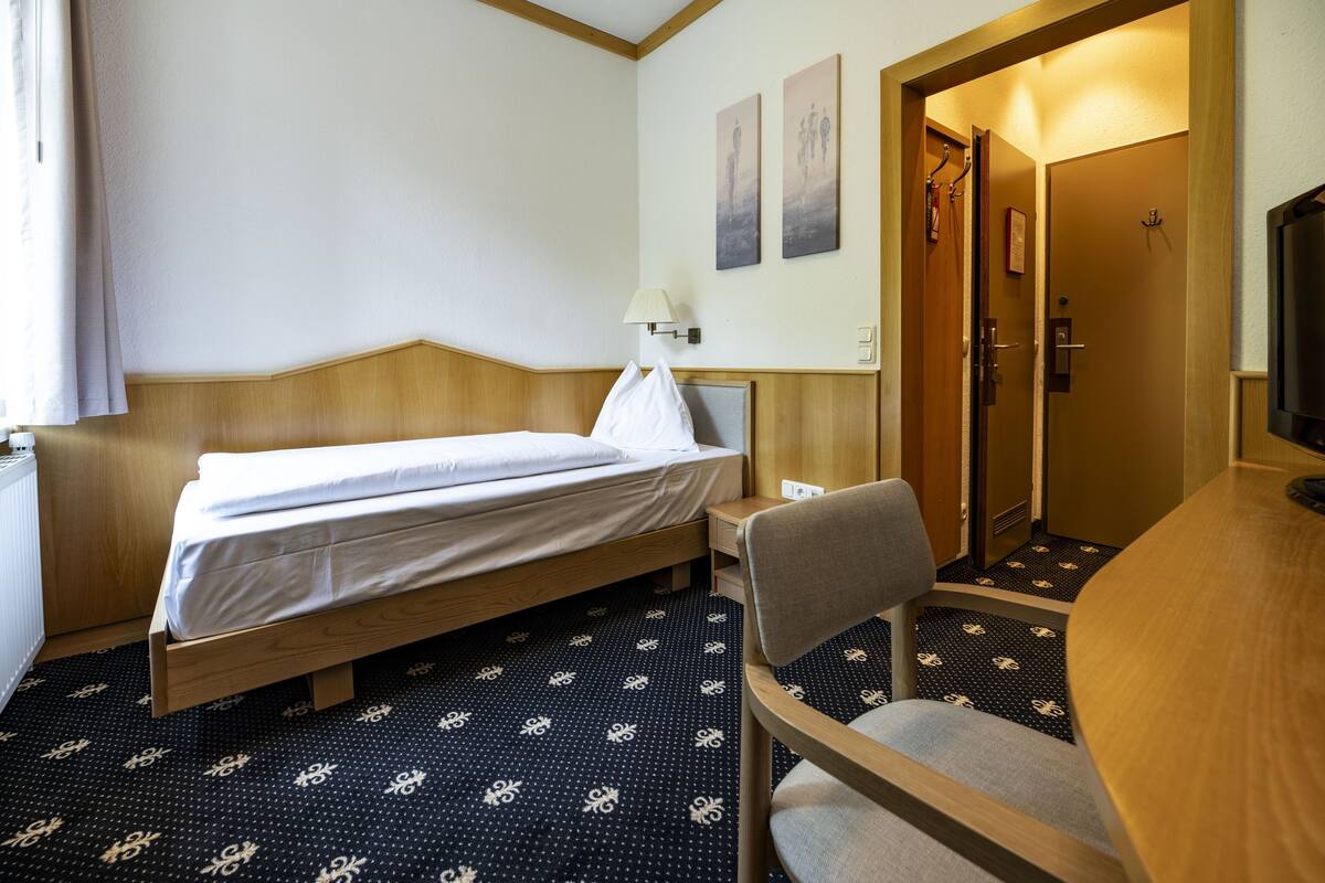 A hotel room with a bed, a chair, a desk, and a TV.