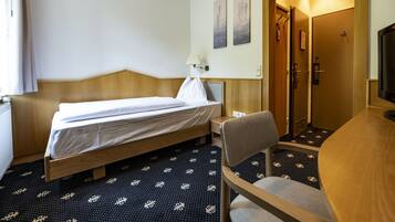 A hotel room with a bed, a chair, a desk, and a TV.