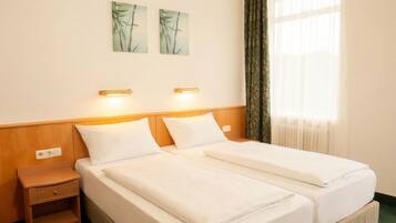A hotel room with a double bed, two bedside tables, a nightstand, and a window with curtains.