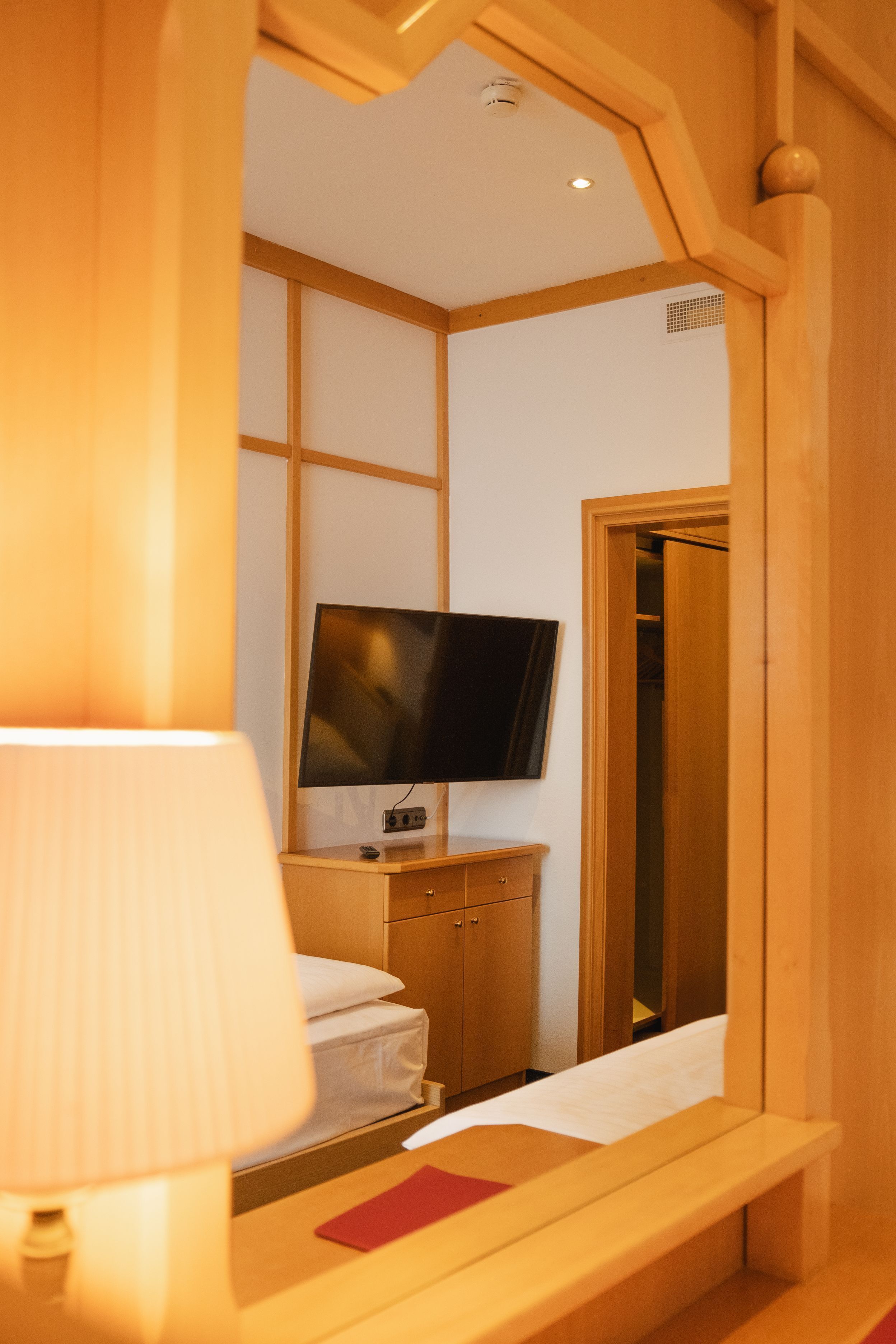 Una habitación de hotel con una cama, un televisor sobre un soporte de madera, una mesita de noche y un armario.