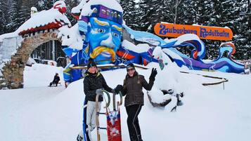 A snow-covered outdoor area with a large, colorful sculpture and a sign that reads "Zugerberg Rodelbahn".