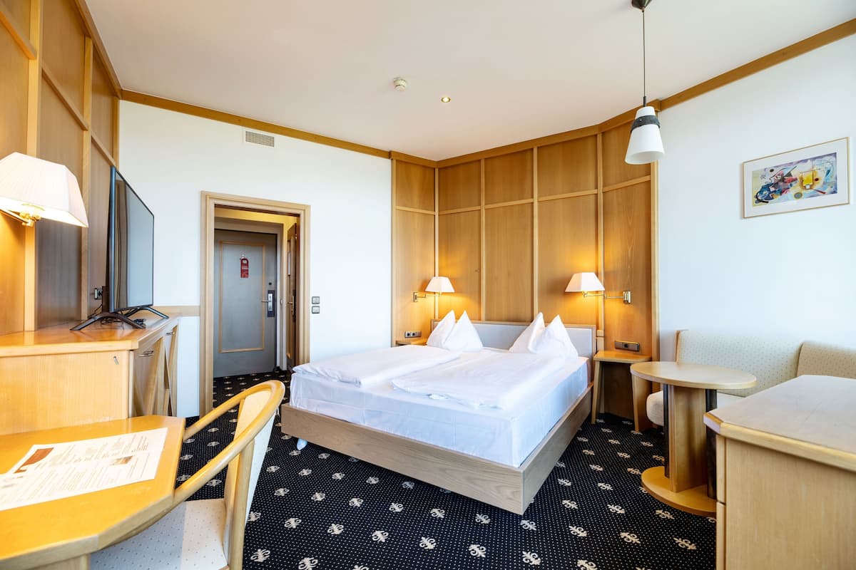 A hotel room with a bed, two bedside tables with lamps, a desk with a chair, a small table, and a sofa.