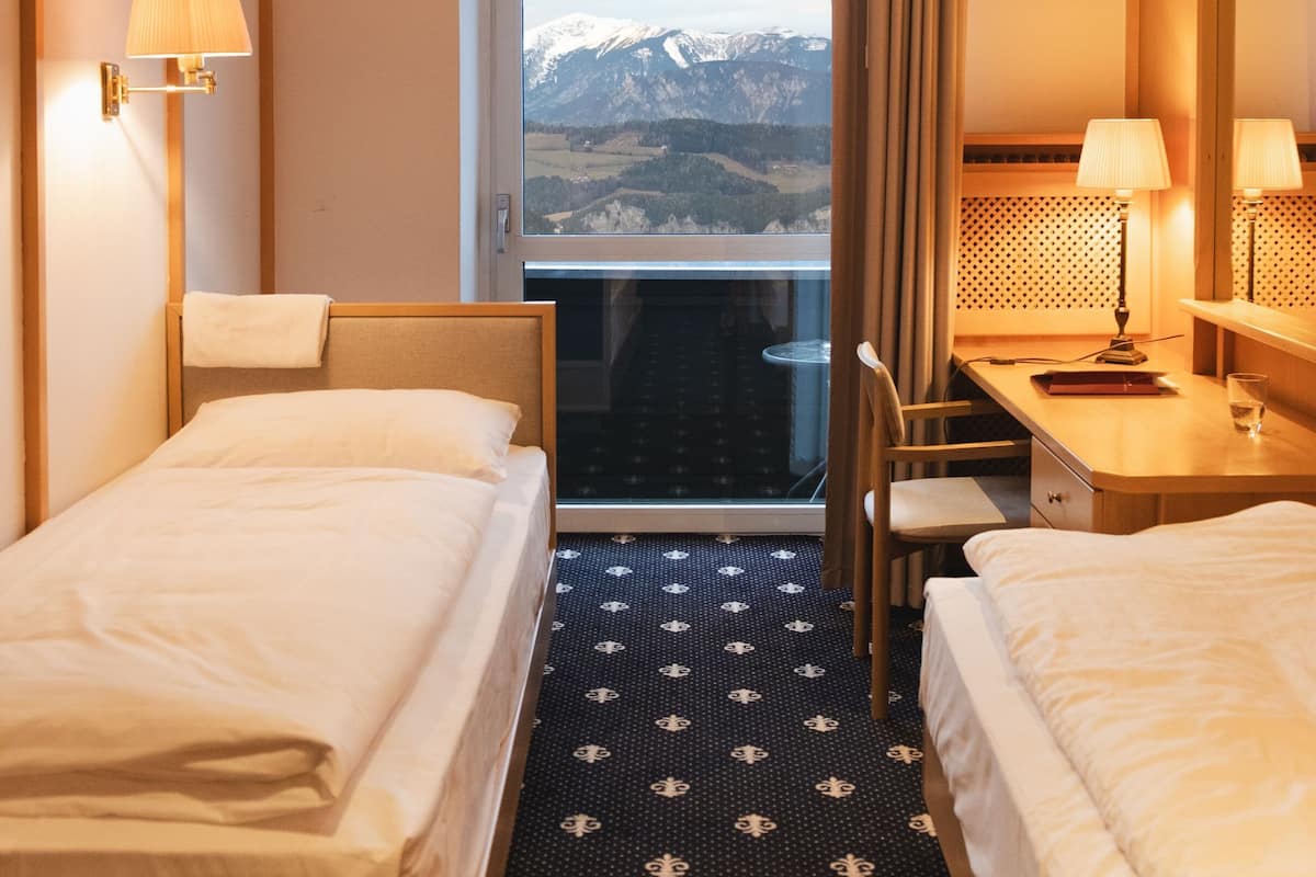 A hotel room with two beds, a desk, and a view of mountains through a window.