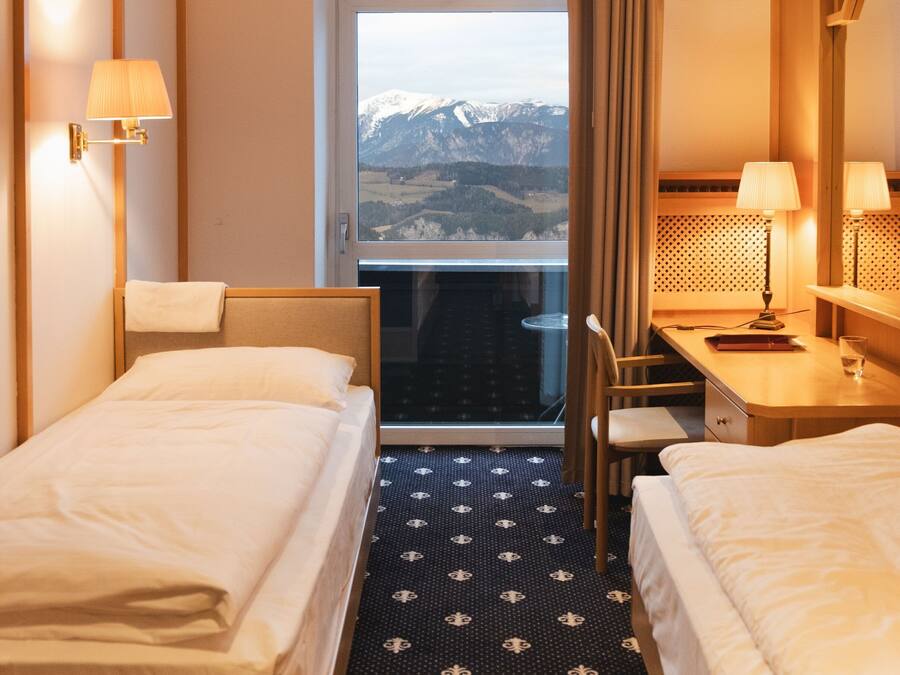 Una habitación de hotel con dos camas, un escritorio y vistas a montañas a través de una ventana.
