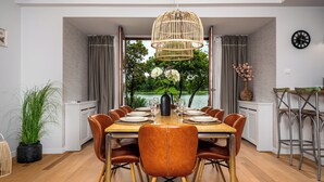 Un comedor con vistas a un lago, una mesa de madera preparada para seis personas y un jarrón con flores.