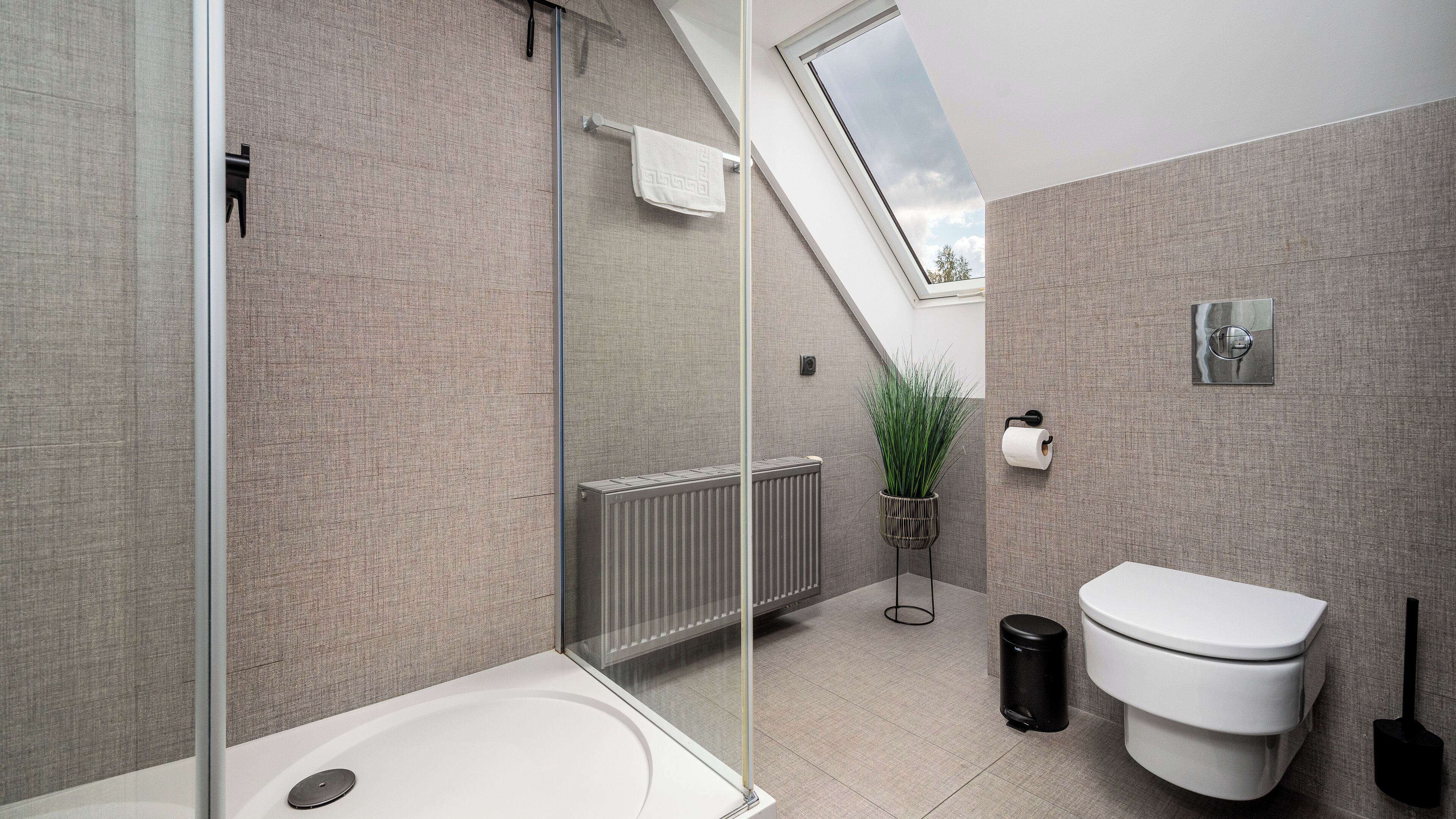 A modern bathroom with a glass shower enclosure, a white toilet, a radiator, and a potted plant.