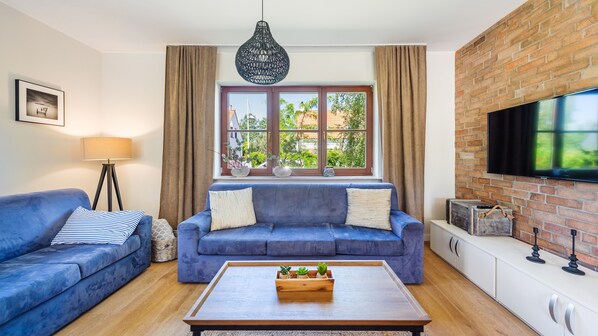 Una sala de estar con un sofá azul, una mesa de centro con plantas, un televisor y una pared de ladrillo.