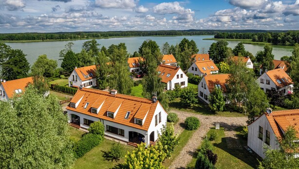 Zona residencial con casas de techos rojos y paredes blancas, rodeada de abundante vegetación y un lago grande.