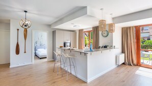 Una cocina moderna con una isla central, taburetes de bar y un comedor con vistas a zonas verdes.