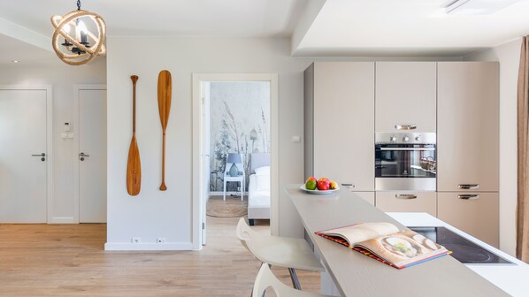 A modern kitchen with a built-in oven, a dining area with a table and chairs, and a hallway with wooden paddles on the wall.