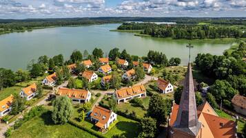 A lakeside village with houses featuring red-tiled roofs, surrounded by lush greenery and a prominent church steeple.