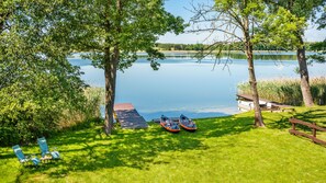 A lakeside view with a dock, two canoes, and a picnic table.
