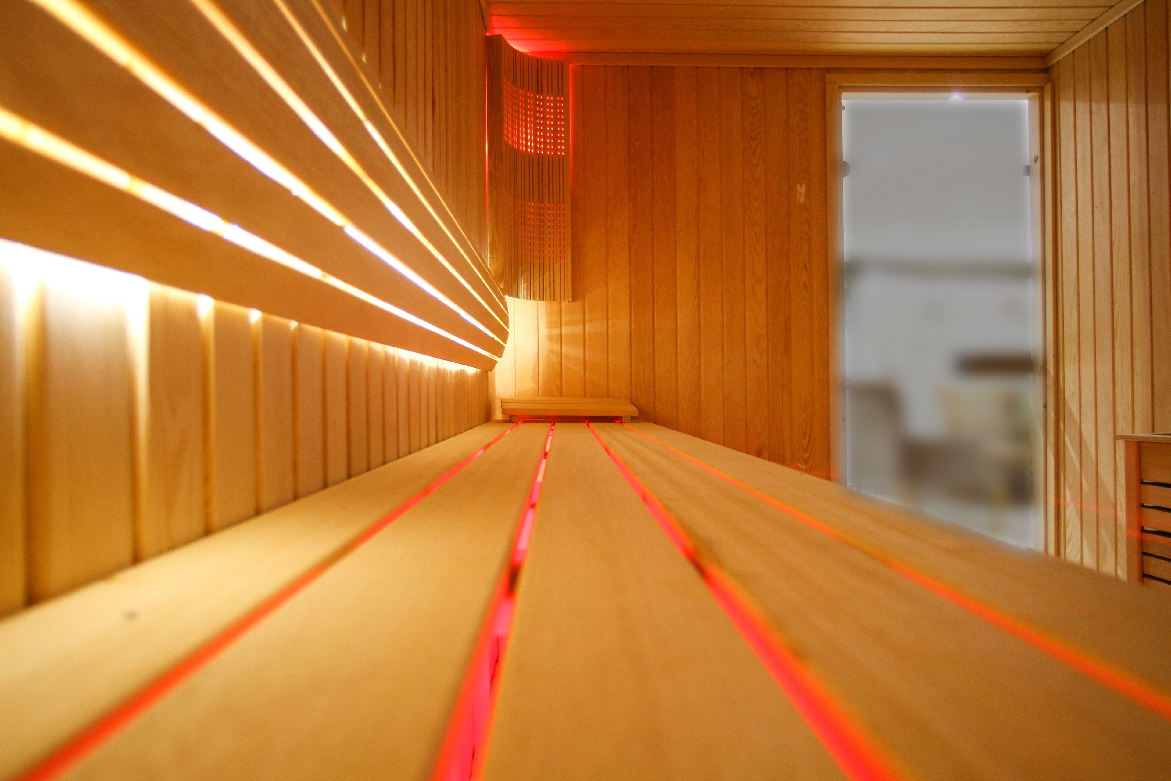 A sauna with wooden walls and benches, a visible door, and a ceiling with light fixtures.