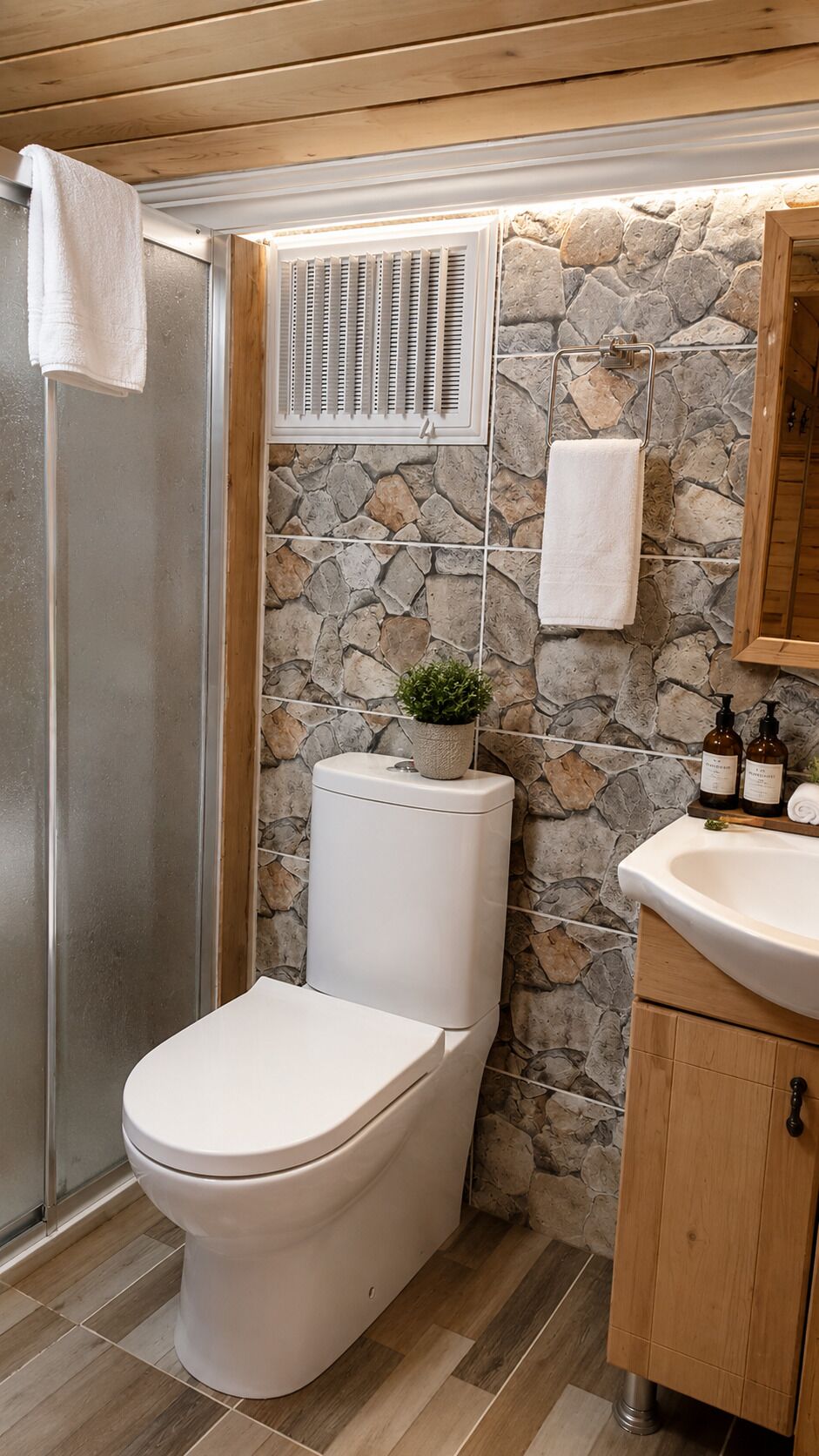 A bathroom with a stone wall, a toilet, a sink, and a shower area.