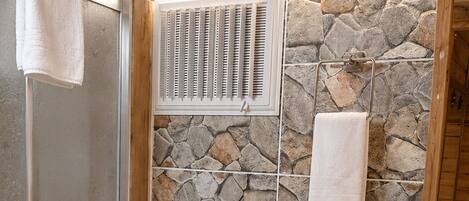 A bathroom with a stone wall, a toilet, a sink, and a shower area.