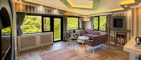 Una sala de estar moderna con sofá, sillones, televisor y ventanas amplias con vista a follaje.