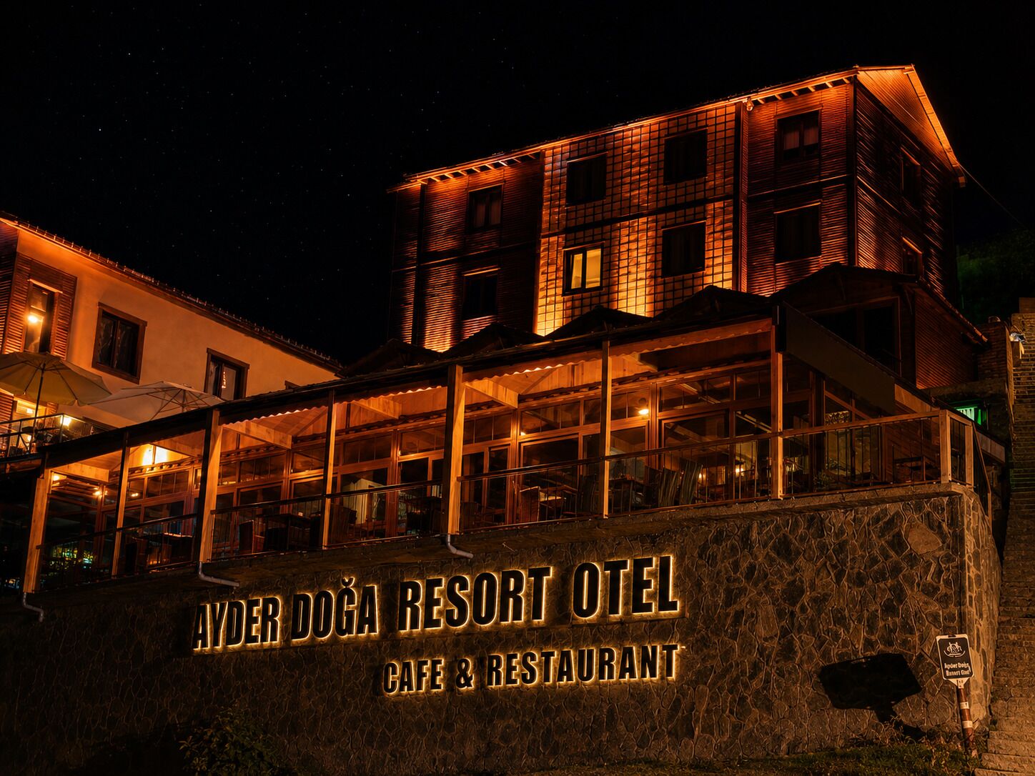 A building with a sign reading 'AYDER DOĞA RESORT OTEL CAFE & RESTAURANT' at night.