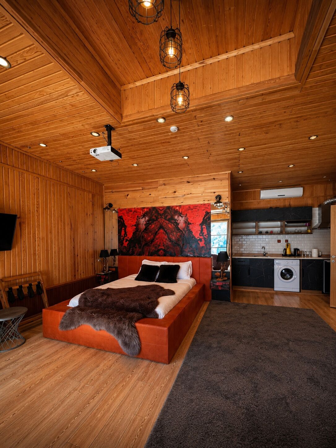 A wooden interior with a bed, a kitchen, and a projector on the ceiling.