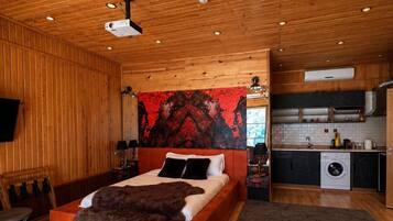 A wooden interior with a bed, a kitchen, and a projector on the ceiling.