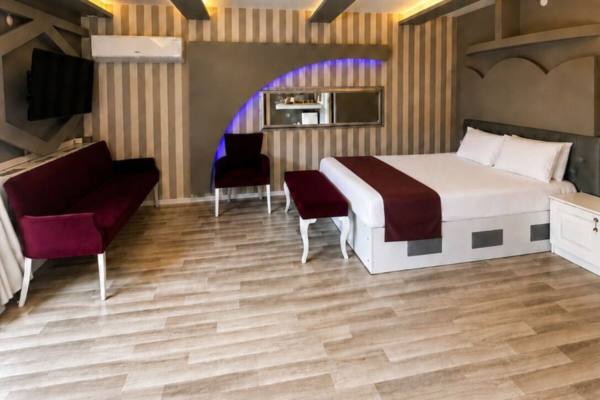 A modern bedroom with a bed, a sofa, a chair, a TV, and an air conditioning unit.