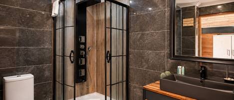 Un baño moderno con ducha envuelta en vidrio, inodoro, tocador con espejo y paredes de mármol oscuro.