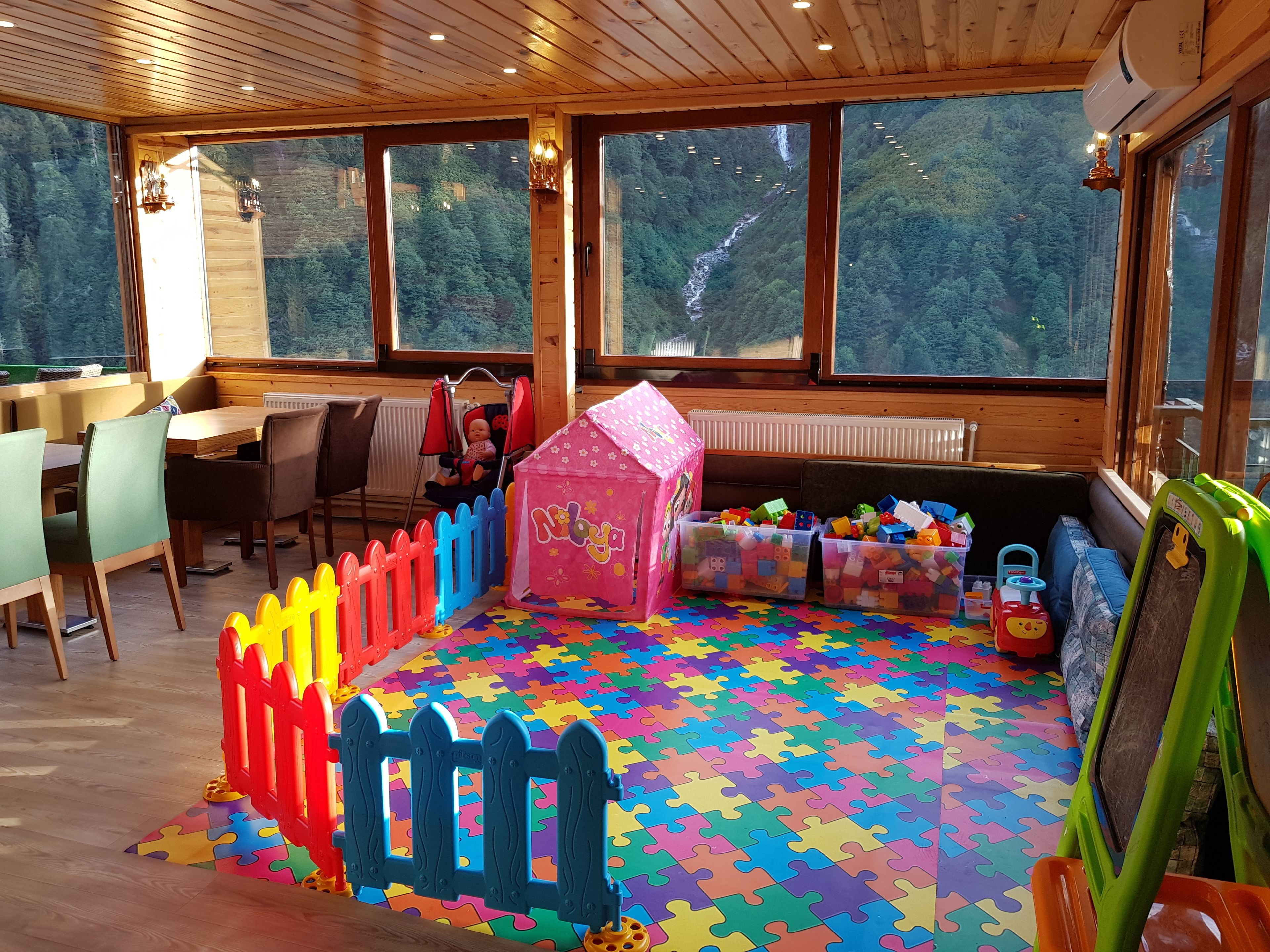 A children's play area with a colorful puzzle floor, a pink playhouse, and a toy train.