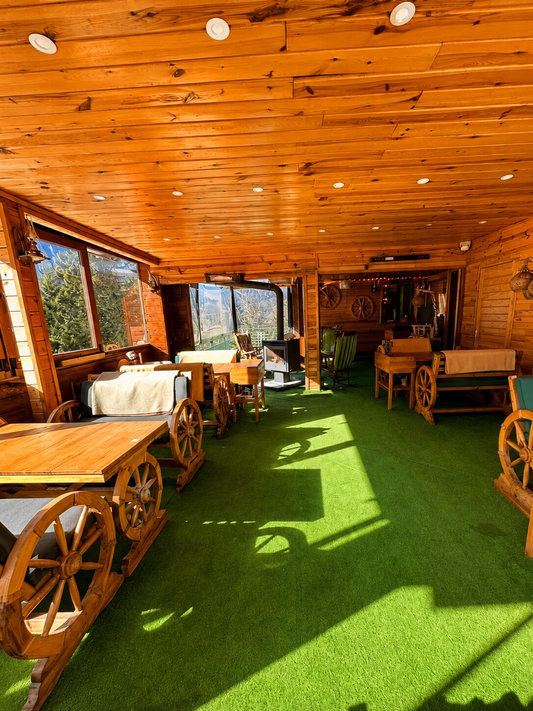 A rustic cabin interior with wooden walls, a green artificial floor, and large windows.