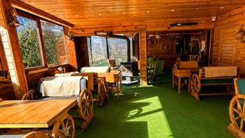 A rustic cabin interior with wooden walls, a green artificial floor, and large windows.