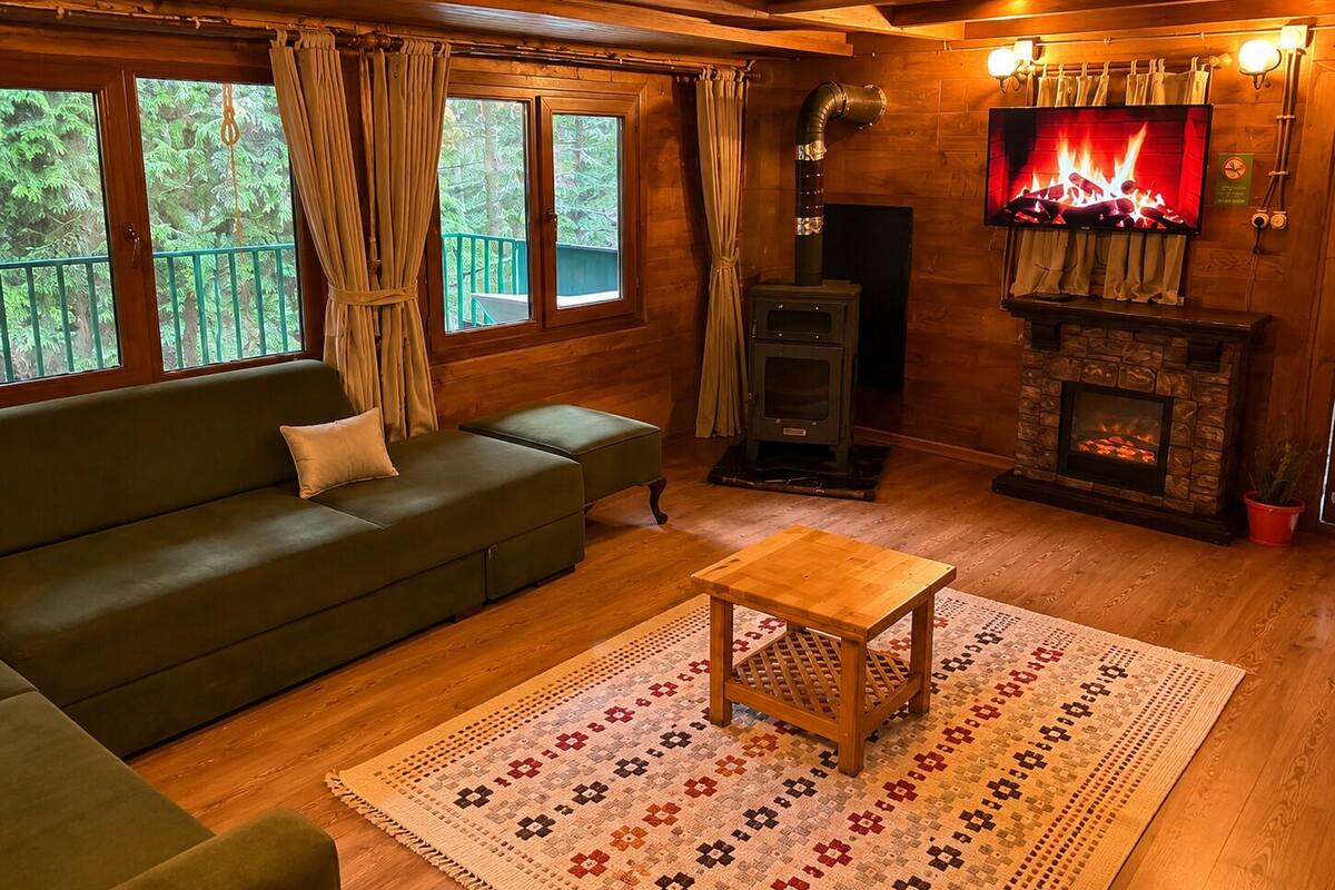 A cozy cabin interior with a sofa, a small table, a fireplace, and a TV displaying a fire.