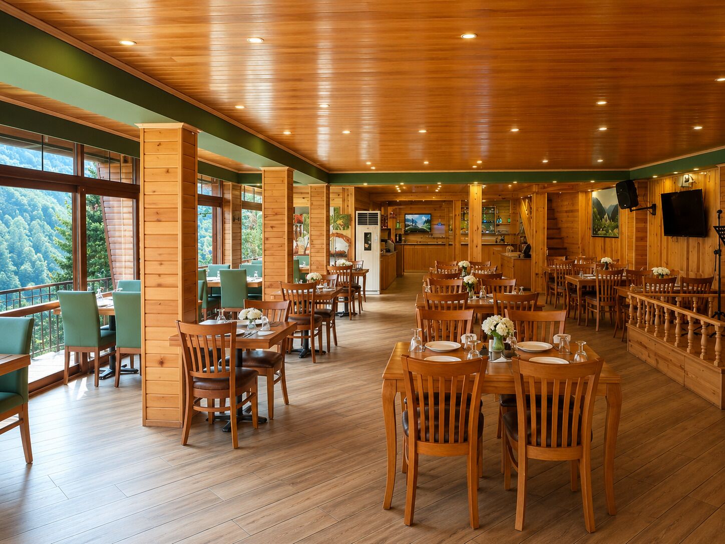 Un comedor amplio con mesas y sillas de madera, ventanas grandes que ofrecen vistas al bosque, y una cocina al fondo.