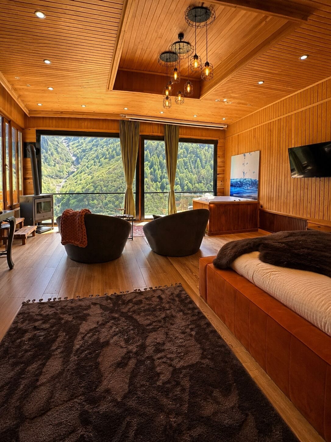 Un interior moderno con paneles de madera, un ventanal con vistas a un bosque, una chimenea y una zona de estar acogedora.