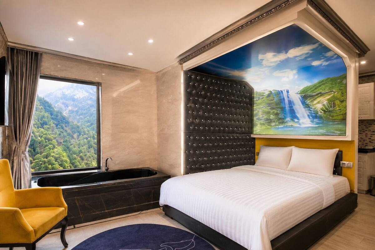 A modern hotel room with a large bed, a bathtub, a yellow armchair, and a scenic mural of a waterfall.