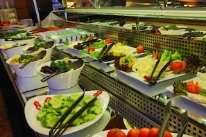 Buffet com diversos alimentos, incluindo saladas, frutas e legumes.