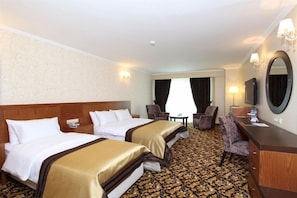 Quarto de hotel com duas camas, uma escrivaninha, uma cadeira, um espelho e piso coberto por carpete.