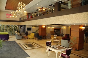 Um hall de hotel com lustre, área de estar e escadaria visível.