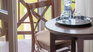 Een houten stoel en tafel met een waterfles en glazen op een dienblad, nabij een glazen deur met uitzicht op groen.