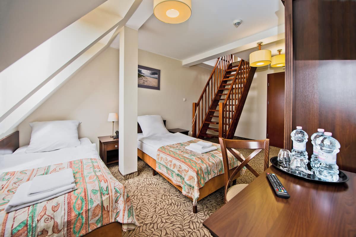 A hotel room with two beds, a wooden staircase, a desk with a remote control, and a tray with water bottles.