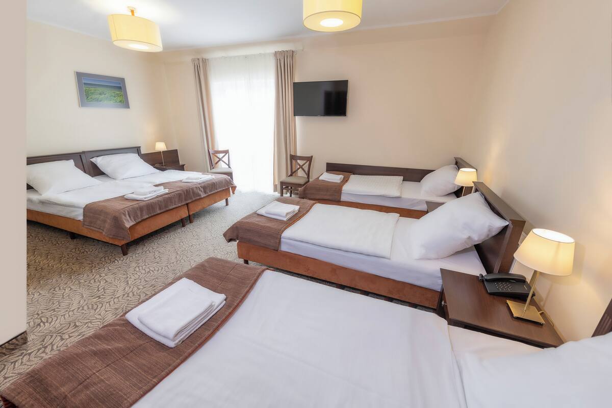 A hotel room with three beds, a flat-screen TV, and a desk with a telephone.