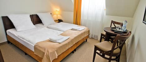 A hotel room with two beds, a small table with a chair, and a lamp.