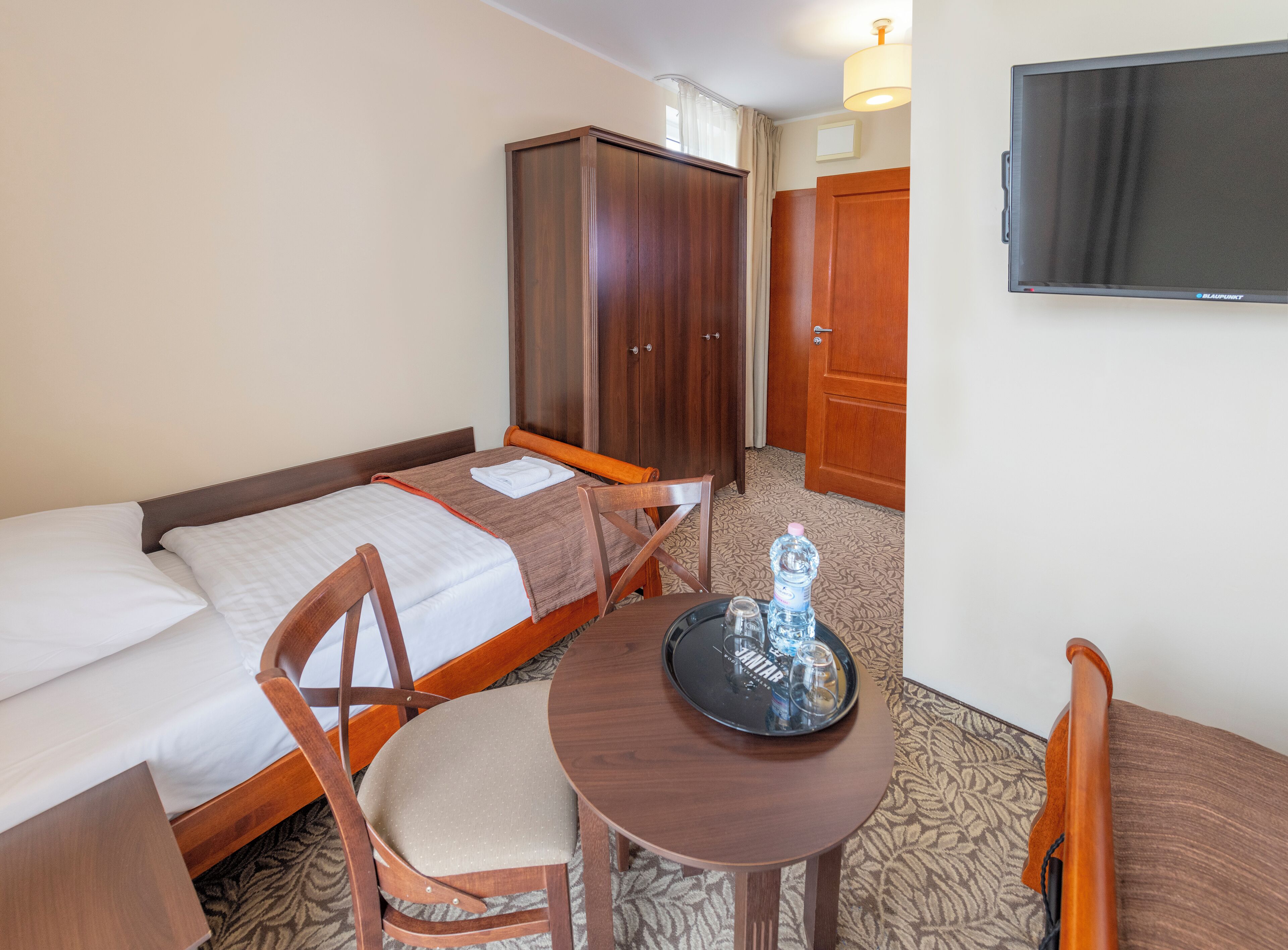 Habitación de hotel con cama, armario de madera, mesa con bandeja y televisor en la pared.